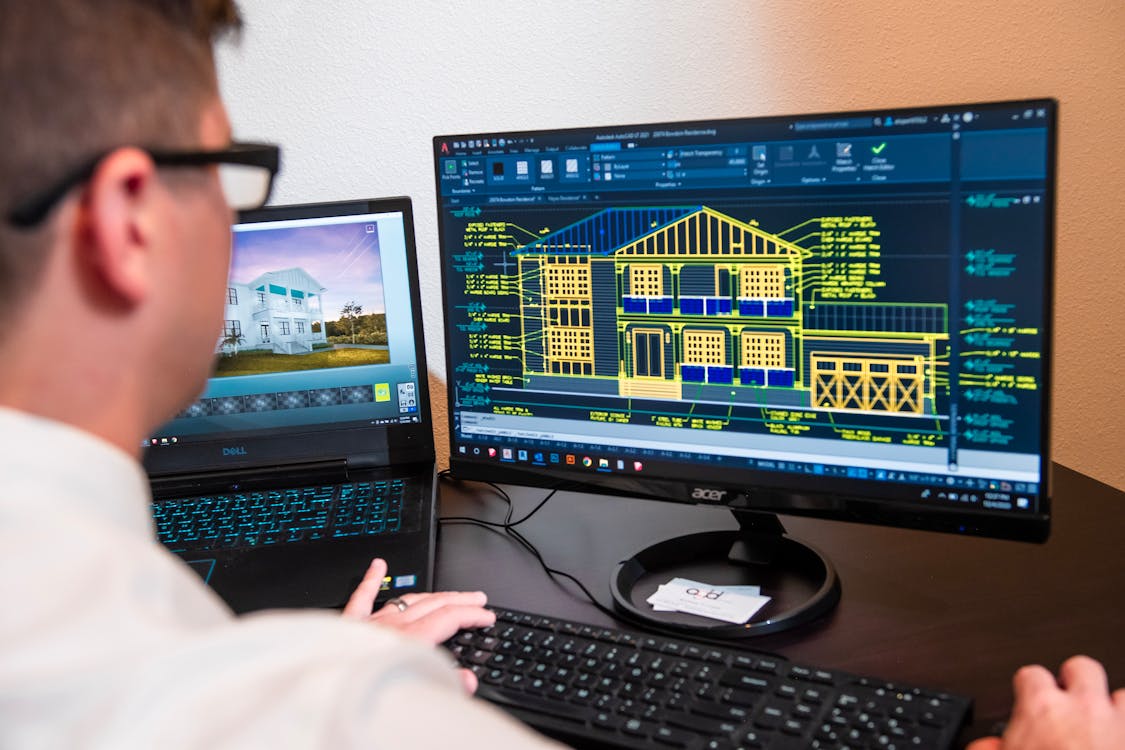 Architect working with CAD software showing building wireframe on dual monitors